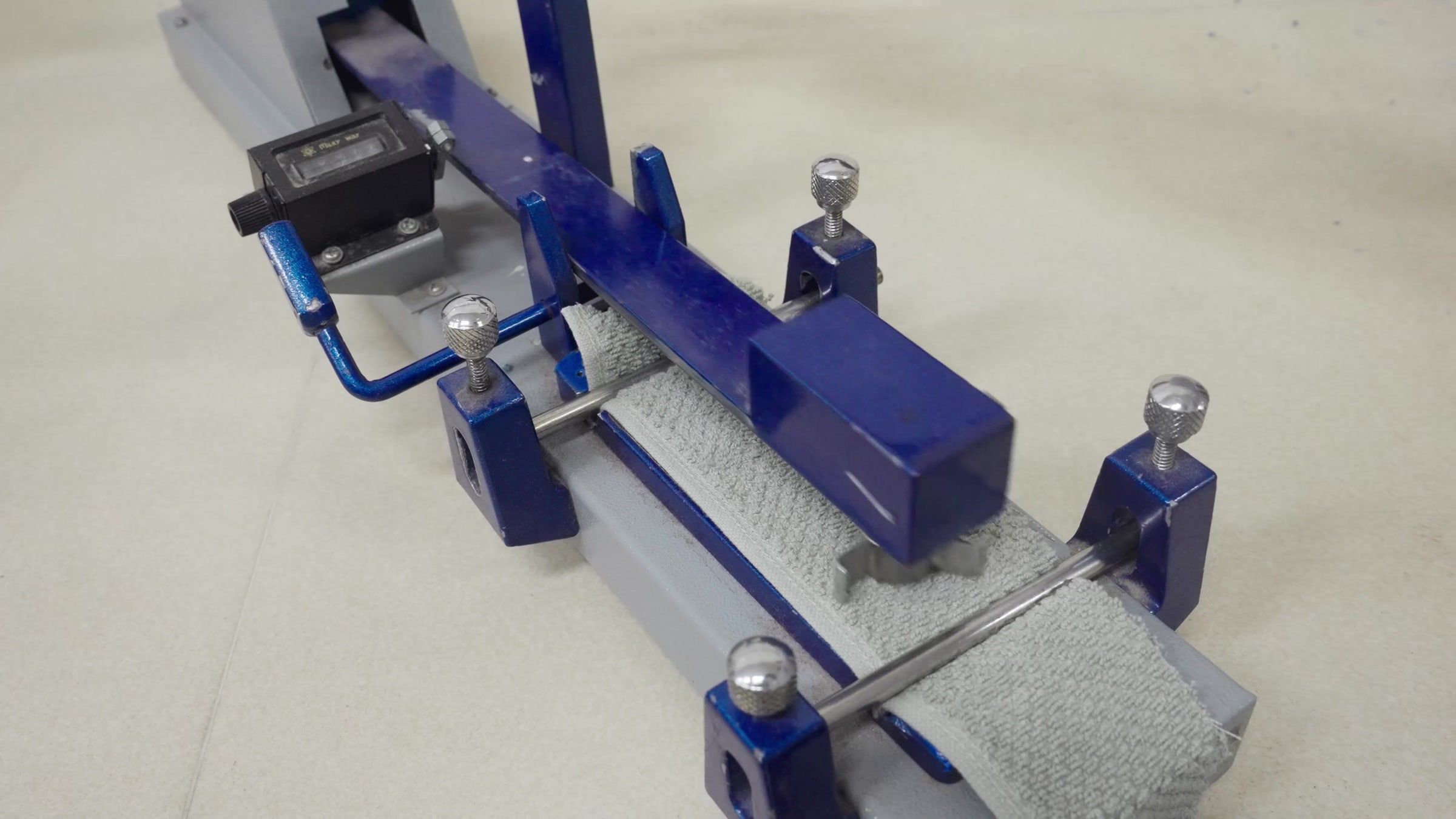A crockmeter, its white test cloth clamped over a grey towel.