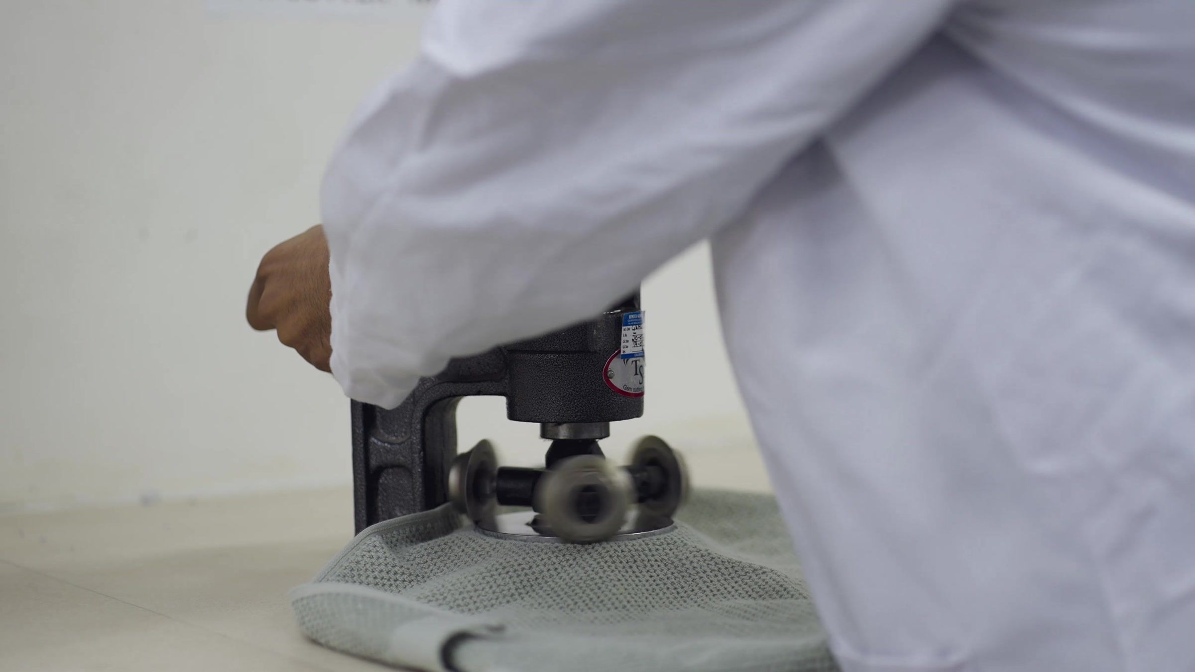 A technician in a white coat working the GSM cutter on a piece of cloth.