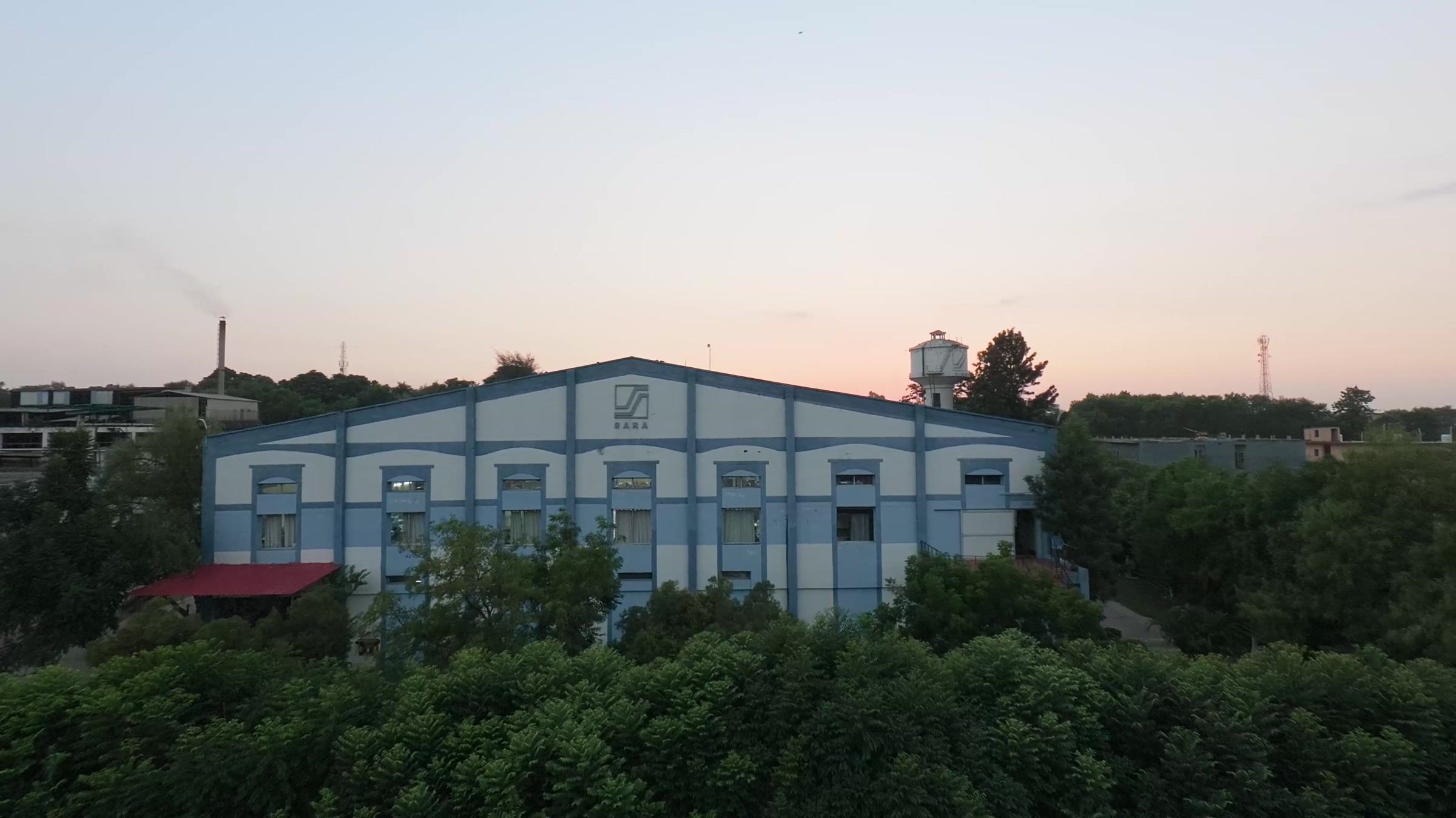 The plant at Nalagarh at dusk, the sheds and the water tower above the trees.